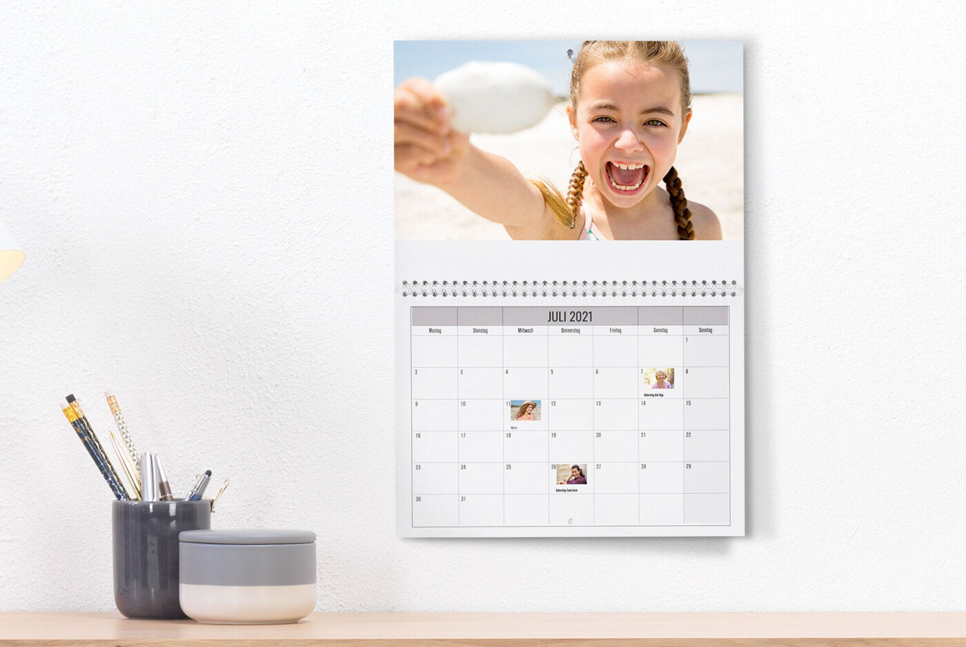A wall calendar shows a happy snapshot of a child holding a shell at the beach.