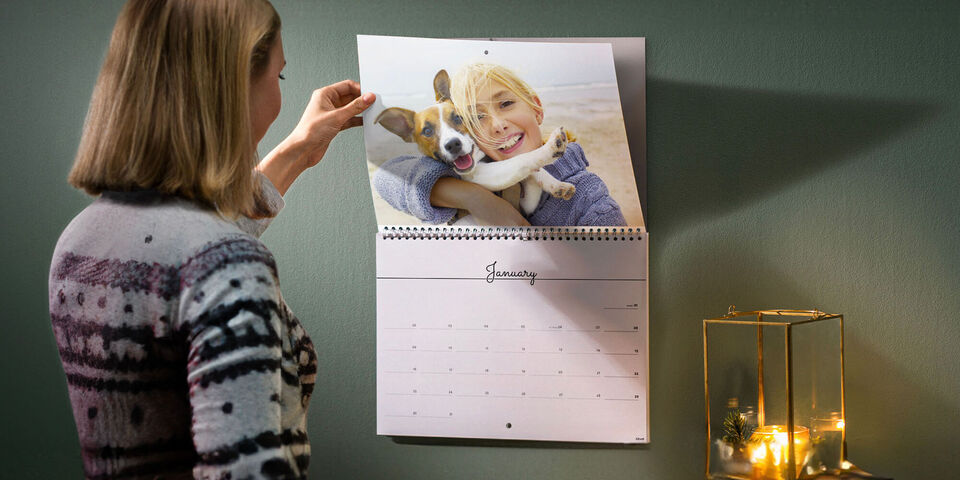 Wall calendar with a dog image is being flipped through.