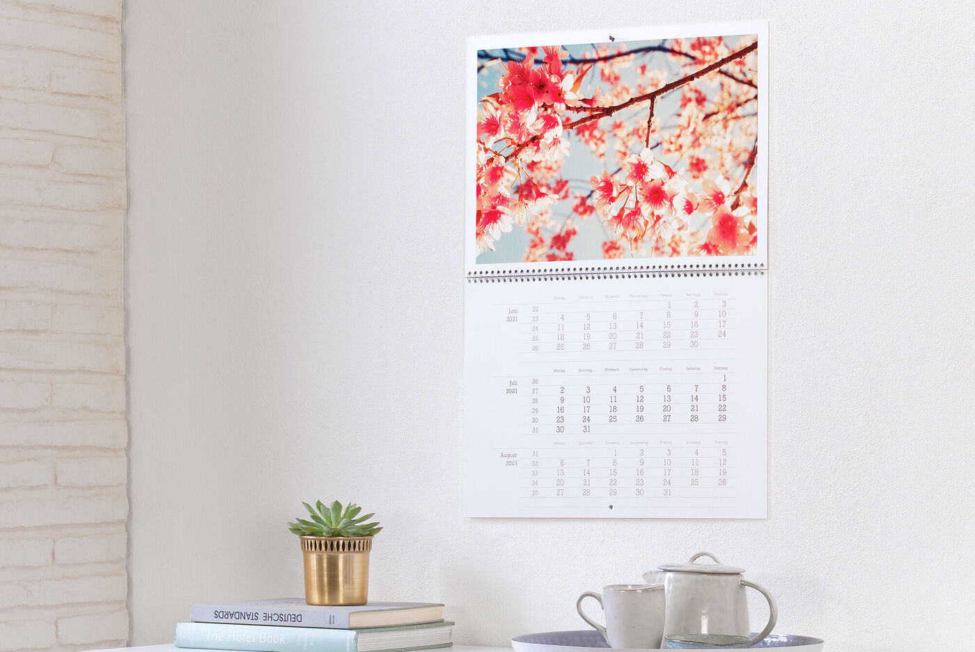 A CEWE photo calendar with cherry blossoms in the background, hanging on a white wall.